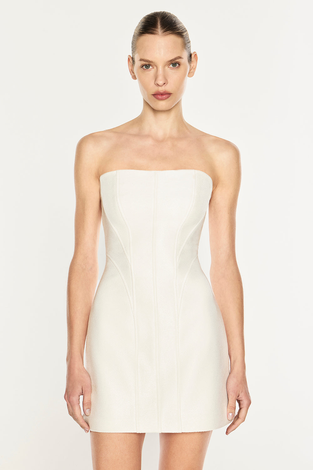 A model wearing a strapless, off-white mini dress with structured seams, photographed against a plain light background.