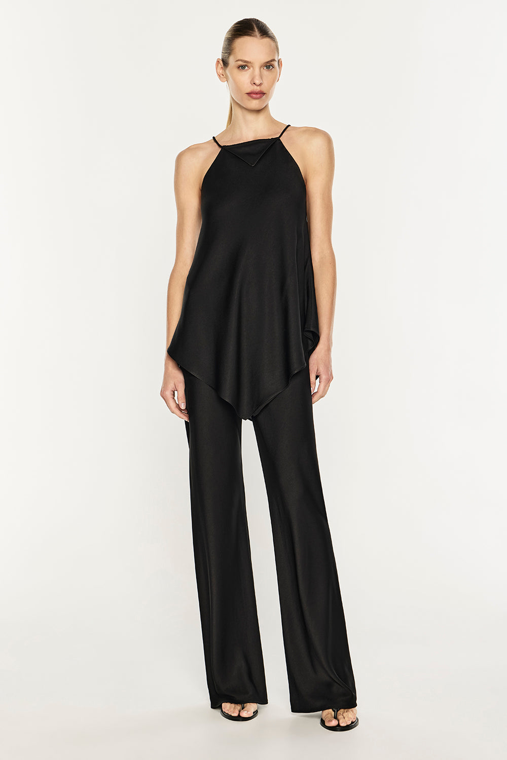 A model wearing a black satin halter top and matching wide-leg trousers, standing against a plain white studio background.