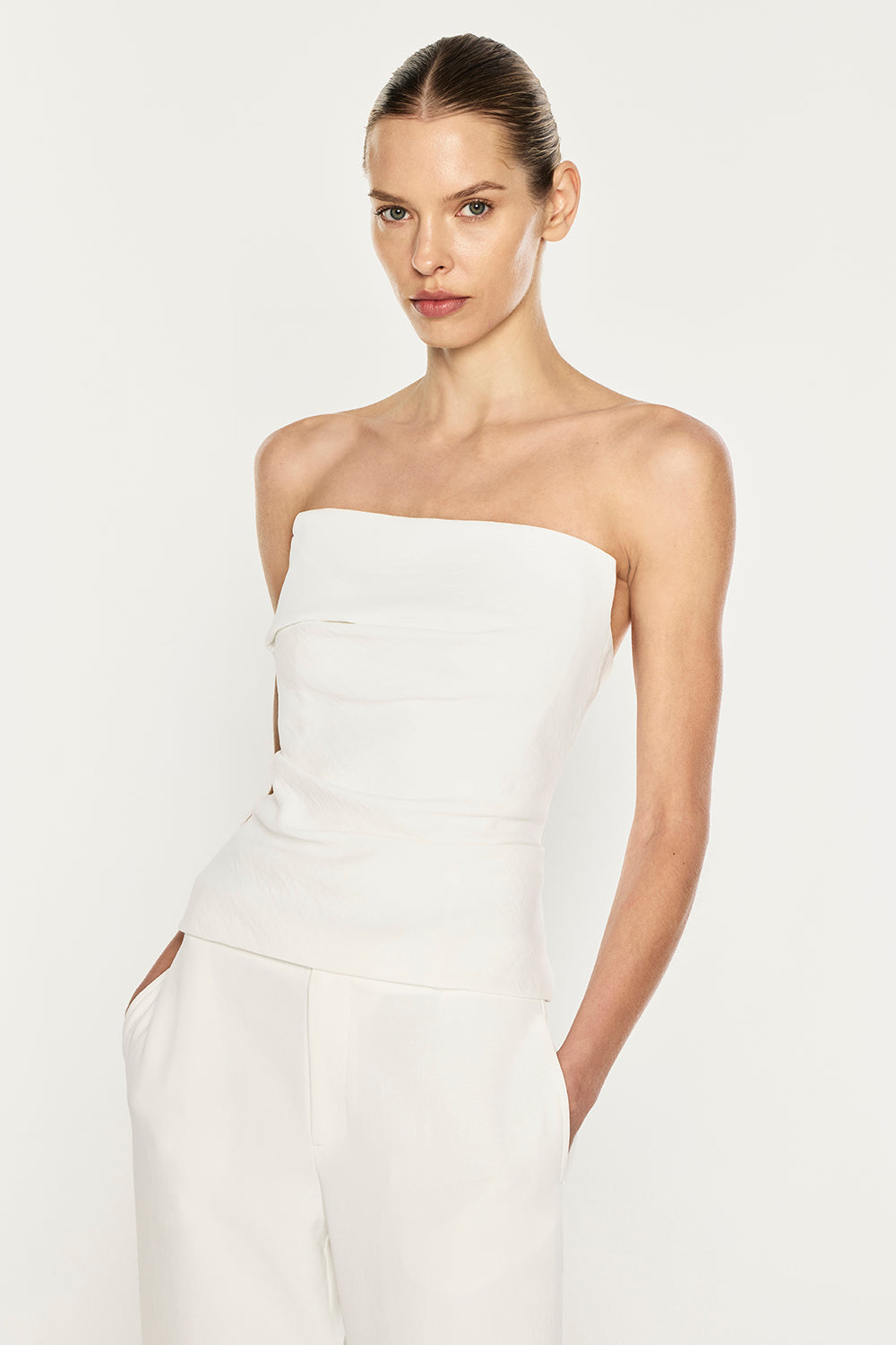 A model wearing a white strapless tube top and matching white trousers, photographed against a clean white studio background.