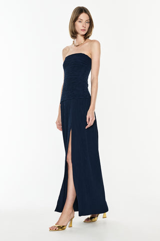 Wearing a strapless navy gown with a high slit on a white background