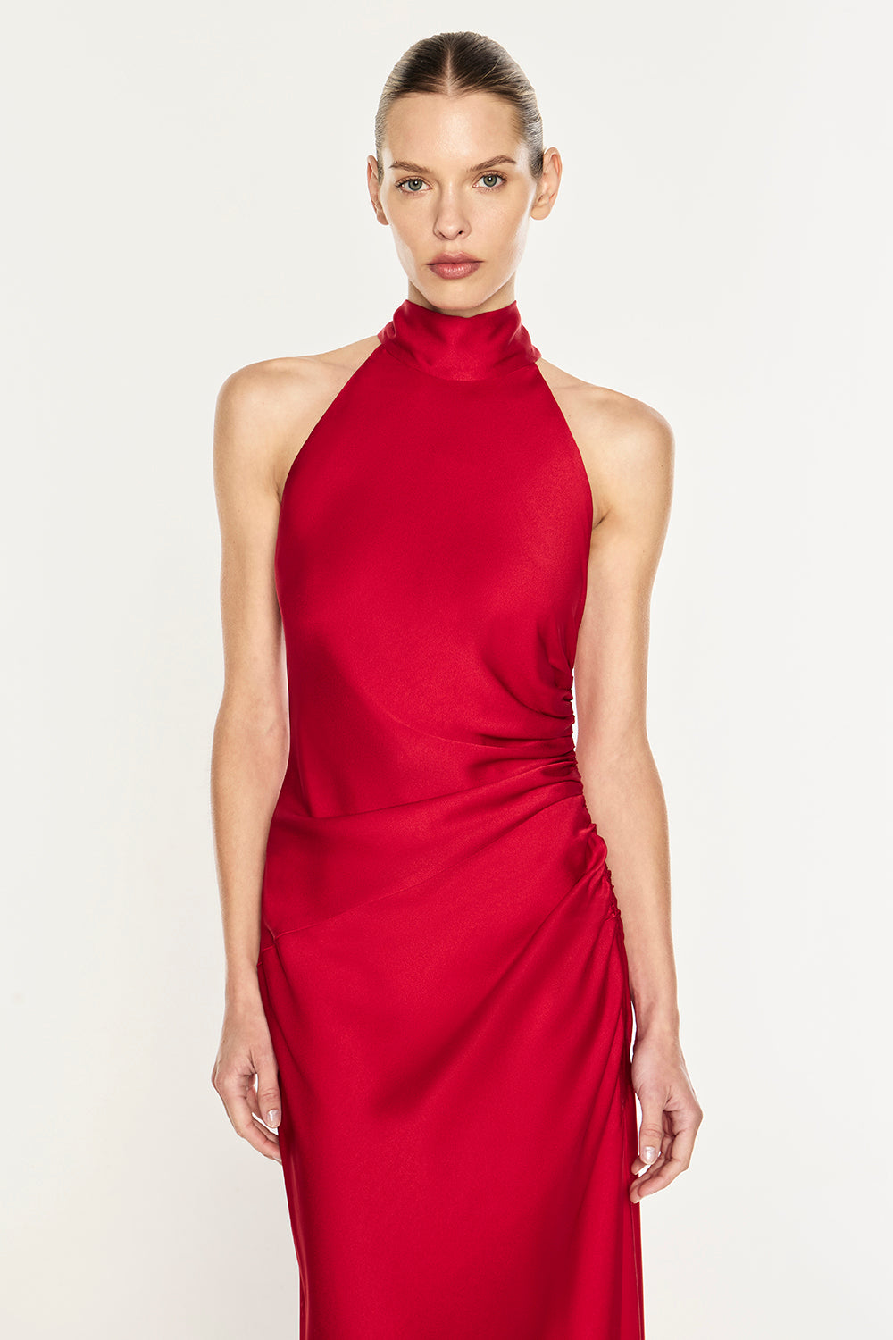 A model wearing a vibrant red halter-neck midi dress with draped side detailing, photographed against a clean white studio background.